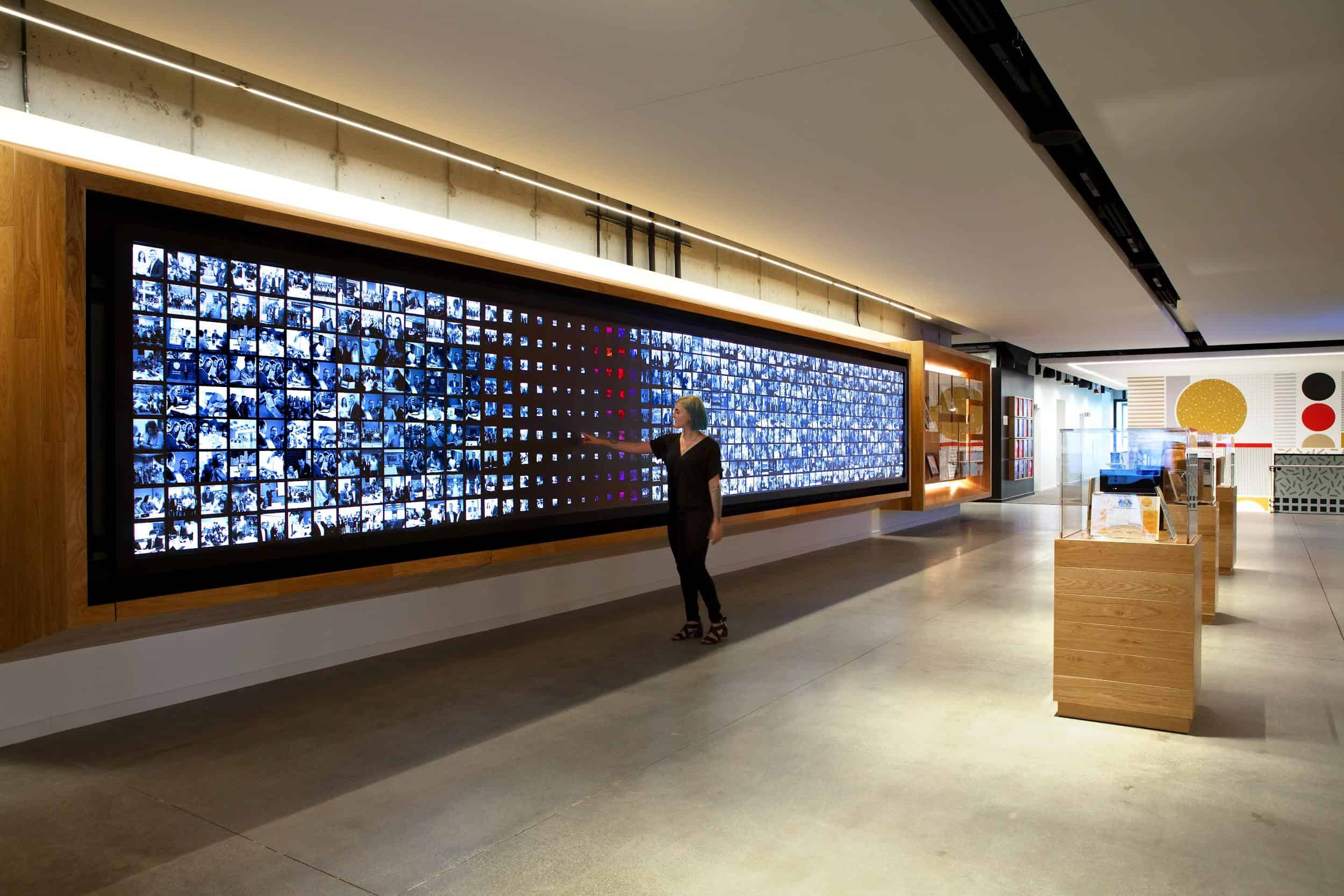 Modern exhibit with digital display of small images, interactive screen, wooden accents, and high-tech artistic vibe.